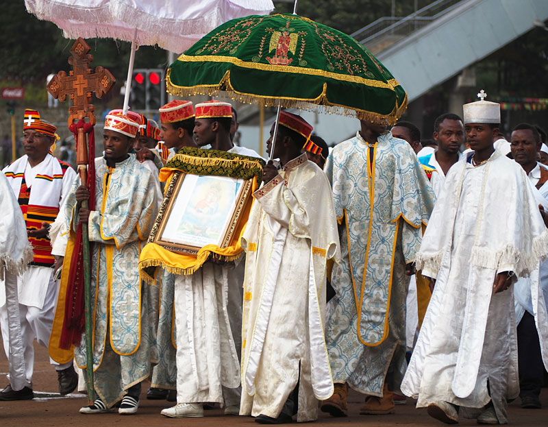 Priests protect a sacred icon with richly decorated parasols.