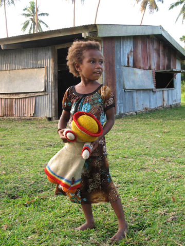 A girl and her doll outside her home in the Maskelyne Islands