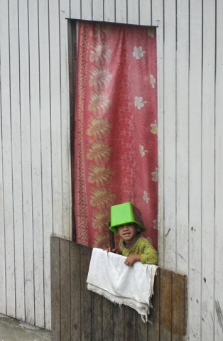 A boy wearing a bucket peeks from a house in Neiafu, Vava’u