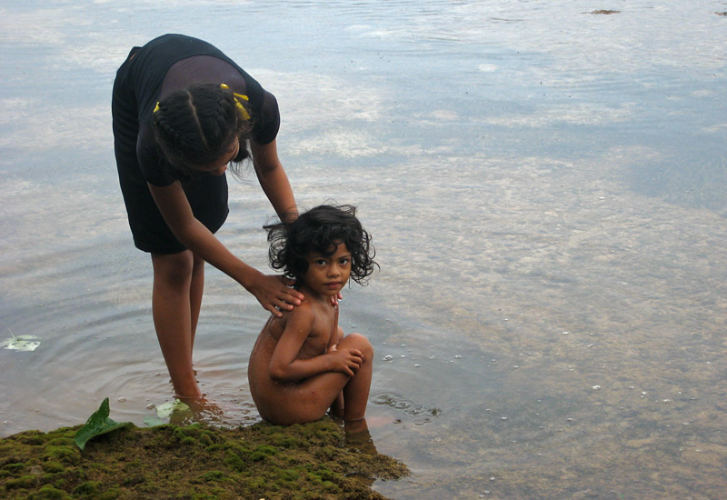 A girl washes her sister in a rock pool at Toula village, Vava’u