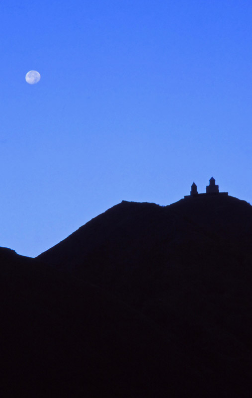 The moon rises behind the 14th century Tsminda Sameba Church near Kazbegi