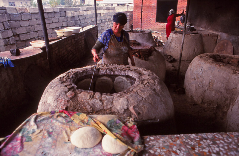 Women bake bread by sticking the dough to the sides of wood-fired ovens